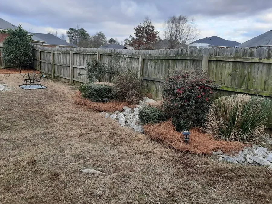 Pine straw bed with shrubs beside a wood fence