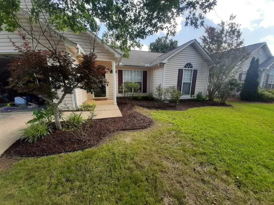 Front yard of a brick house with dark mulch beds
